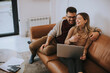 © BGStock72 - Young couple using laptop together while sitting on sofa at home