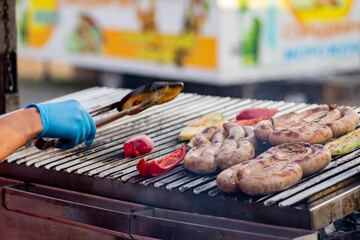 Wall Mural - Cook turns over the grilled sausage and vegetables. Street food. BBQ picnic