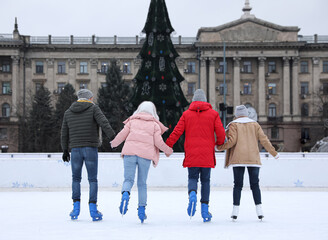 Canvas Print - Group of friends skating along ice rink outdoors, back view