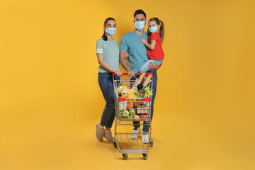 Poster - Family with protective masks and shopping cart full of groceries on yellow background