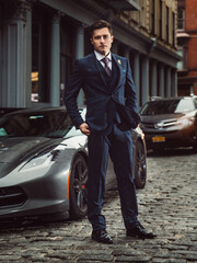 young successful entrepreneur man standing near sport luxury car wearing a classic suit