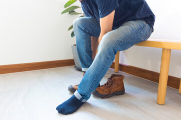 Close up of a young man is put on his leather boots at home foyer.