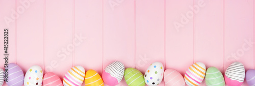 Colorful Easter Egg bottom border over a soft pink wood banner background. Top down view with copy space. © Jenifoto