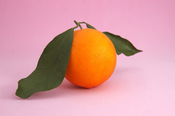 Image of an orange with green leaves on a pink background