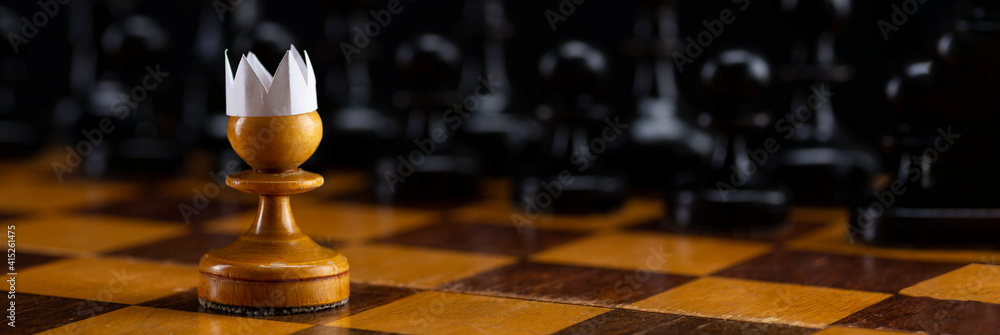 Little brave pawn wearing artificial paper crown suit on chessboard with figures, business entrepreneur leadership concept