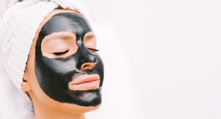 Wall Mural - Beautiful young woman with black purifying charcoal facial mask. Cosmetic procedures, mask for skin care in spa salon. Copy space