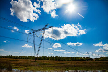 High-voltage transmission line and electric towers (poles) on beauty landscape and sky with clouds and sun.