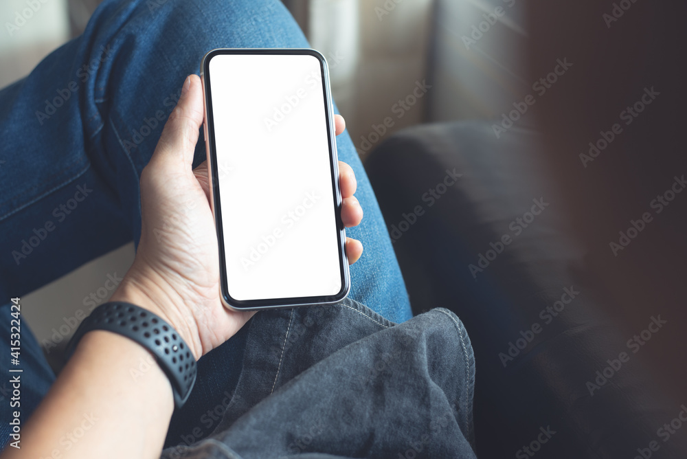 Mockup image of mobile smartphone with blank screen template, man sitting on sofa, hand holding and looking at mobile phone screen - obrazy, fototapety, plakaty 