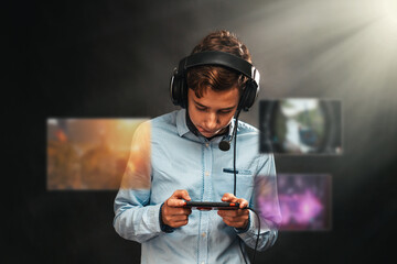 Portrait of a teenage boy in headphones playing a game on his smartphone. Transparent screens with games in front of the player. Black background. Copy. Concept of entertainment and technologies