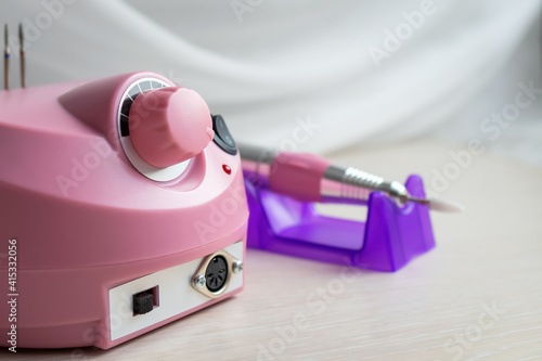 Close-up and selective focus of pink electric machine with special drill pen for hardware manicure and pedicure. Professional equipment for nail service master. Women\'s care and beauty procedures.