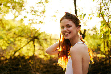 happy red-haired woman on nature in the forest near green trees Summer sun