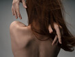 Back view of sexy red-haired woman naked back touching with hands