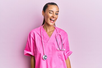 Wall Mural - Young hispanic woman wearing doctor uniform and stethoscope winking looking at the camera with sexy expression, cheerful and happy face.