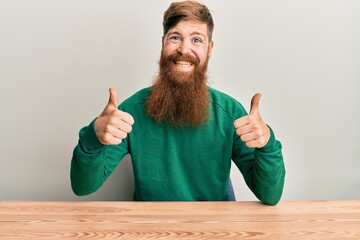 Sticker - Young irish redhead man wearing casual clothes sitting on the table success sign doing positive gesture with hand, thumbs up smiling and happy. cheerful expression and winner gesture.