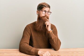 Poster - Young irish redhead man wearing casual clothes and glasses sitting on the table thinking concentrated about doubt with finger on chin and looking up wondering