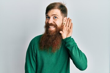 Sticker - Redhead man with long beard wearing casual clothes smiling with hand over ear listening an hearing to rumor or gossip. deafness concept.