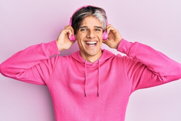 Sticker - Young hispanic man listening to music using headphones looking positive and happy standing and smiling with a confident smile showing teeth