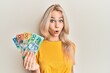 © Krakenimages.com - Beautiful caucasian blonde girl holding australian dollars scared and amazed with open mouth for surprise, disbelief face
