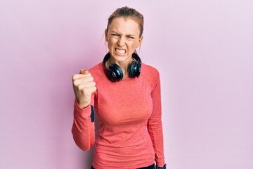 Canvas Print - Beautiful caucasian woman wearing sportswear and arm band angry and mad raising fist frustrated and furious while shouting with anger. rage and aggressive concept.