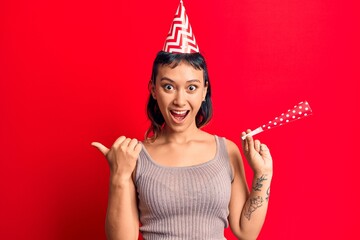 Canvas Print - Young woman wearing birthday hat pointing thumb up to the side smiling happy with open mouth