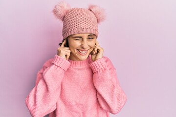 Wall Mural - Young brunette woman wearing cute wool cap covering ears with fingers with annoyed expression for the noise of loud music. deaf concept.