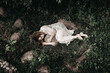 © asauriet - Young lonely woman laying on green grass in white mantle and hugging a huge stone. A mysterious shot from a dark deep forest. Top view