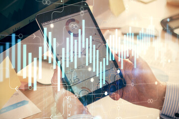 Double exposure of man's hands holding and using a phone and financial graph drawing. Analysis concept.