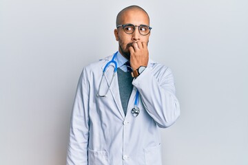 Poster - Hispanic adult man wearing doctor uniform and stethoscope looking stressed and nervous with hands on mouth biting nails. anxiety problem.