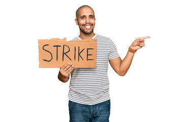 Poster - Hispanic adult man holding strike banner cardboard smiling happy pointing with hand and finger to the side