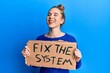 © Krakenimages.com - Young blonde woman holding fix the system banner cardboard smiling and laughing hard out loud because funny crazy joke.