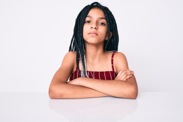 Sticker - Young african american girl child with braids wearing casual clothes sitting on the table relaxed with serious expression on face. simple and natural looking at the camera.