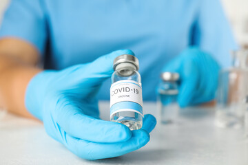 Doctor with coronavirus vaccine at table in laboratory, closeup