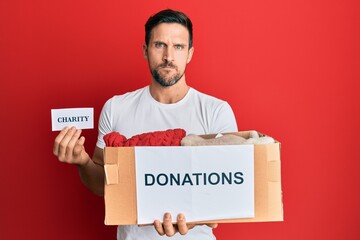 Sticker - Young handsome man volunteer holding donations box with clothes skeptic and nervous, frowning upset because of problem. negative person.