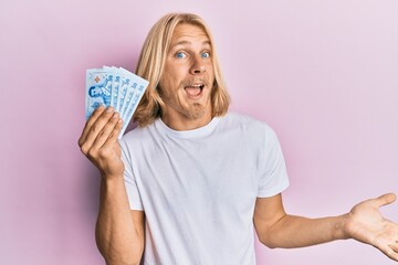 Sticker - Caucasian young man with long hair holding 50 thai baht banknotes celebrating achievement with happy smile and winner expression with raised hand