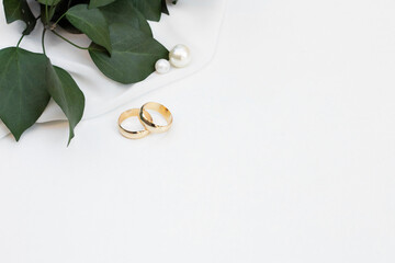 Two gold wedding rings with pearls and green leaves on soft white background