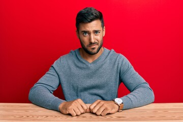Wall Mural - Handsome hispanic man wearing casual style sitting on the table skeptic and nervous, frowning upset because of problem. negative person.
