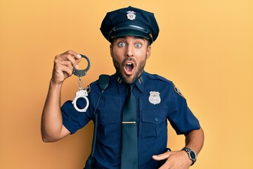 Canvas Print - Handsome hispanic man wearing police uniform holding metal handcuffs scared and amazed with open mouth for surprise, disbelief face