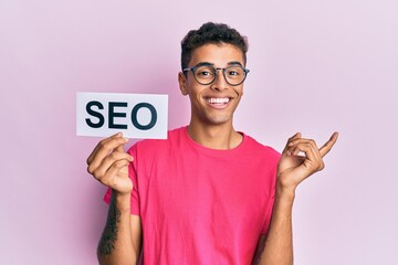 Poster - Young handsome african american man holding seo message paper smiling happy pointing with hand and finger to the side