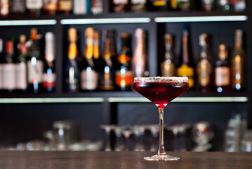 Red cocktail on bar counter. Drink with martini, gin, rum, tequila and fruit on the background of bottles with alcohol. Glass with booze on a wooden board.