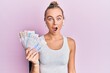 © Krakenimages.com - Beautiful blonde sport woman holding 20 swedish krona banknotes scared and amazed with open mouth for surprise, disbelief face