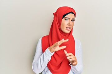 Wall Mural - Young beautiful hispanic girl wearing traditional islamic hijab scarf disgusted expression, displeased and fearful doing disgust face because aversion reaction. with hands raised