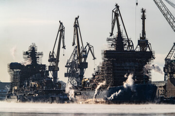  Cranes of of the shipyard on a frosty winter day, steam over the Neva river, smooth surface of the river, mirror reflection on the water, ships under construction, trawlers, nuclear icebreakers