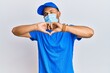 © Krakenimages.com - Handsome man with beard wearing courier uniform and medical mask smiling in love doing heart symbol shape with hands. romantic concept.