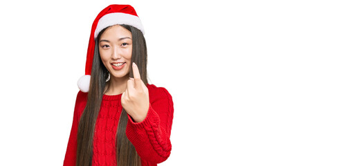 Wall Mural - Young chinese woman wearing christmas hat beckoning come here gesture with hand inviting welcoming happy and smiling