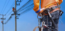 Rear View Of Electrician With Safety Belt And Work Tools Is Preparing To Work On High Altitude With Blurred Background Of Electrical Workers Team Are Working On Power Poles Against Blue Sky