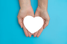 Holding A White Heart On A Blue Background Close-up. The Concept Of Support And Charity
