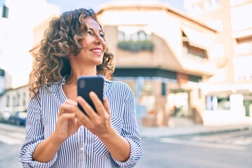 Wall Mural - middle age hispanic woman smiling happy and using smartphone at the city.