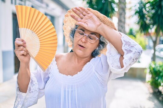 middle age woman with grey hair using handfan on a very hot day of a heat wave
