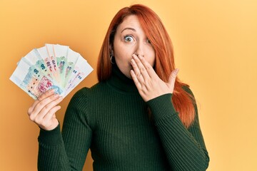 Sticker - Beautiful redhead woman holding singapore dollars banknotes covering mouth with hand, shocked and afraid for mistake. surprised expression