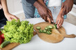 © sofiko14 - Close up cropped image of hands of black daddy teaching his teenage daughter holding knife and cut fresh cucumber. Healthy food with family lifestyle
